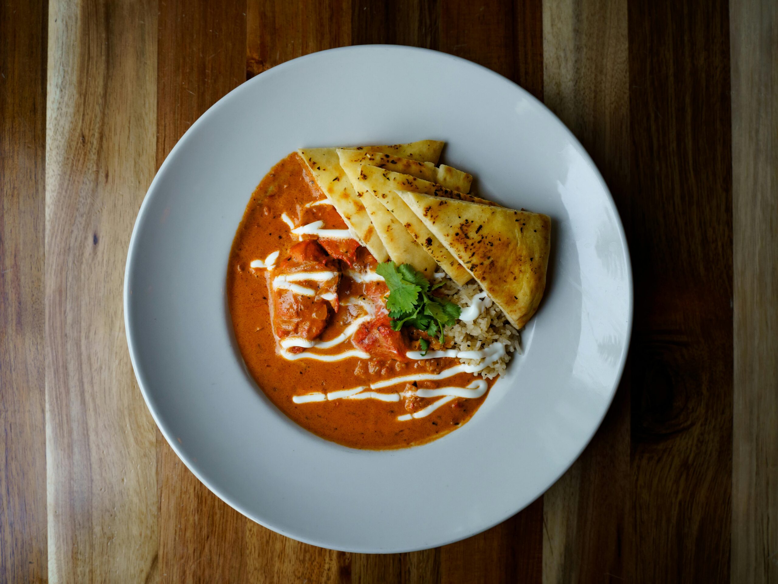 Top view of a flavorful butter chicken dish served with naan and garnished with cilantro.