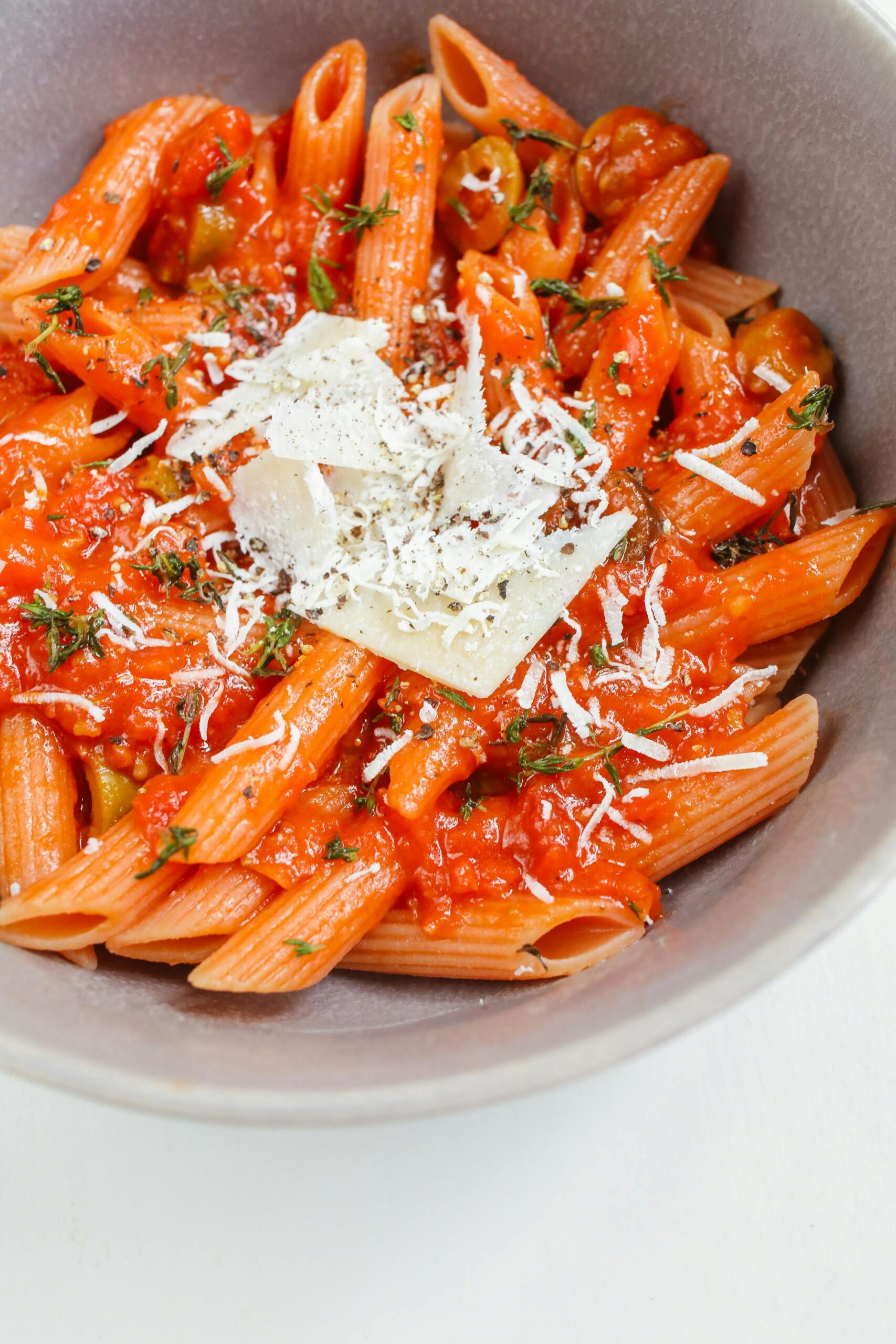 Close-up of penne pasta in rich tomato sauce topped with cheese, perfect for an Italian meal.